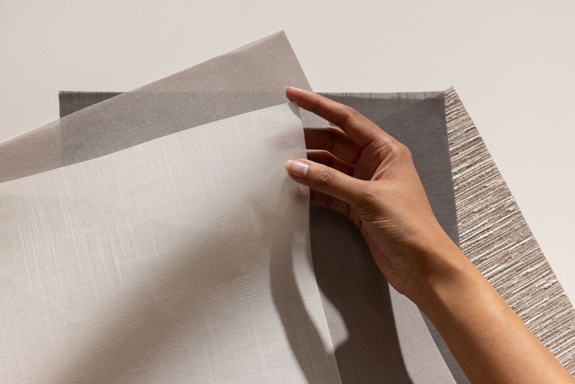 A hand holding several roller shade fabric swatches